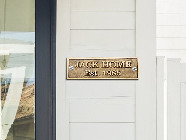 May include: A brass plaque with the text "JACK HOME Est. 1985" mounted on a white wooden wall.