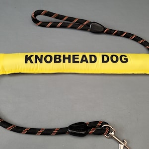May include: A yellow padded dog lead with black and orange rope and a metal clip. The lead has the text "KNOBHEAD DOG" printed on the padded section.
