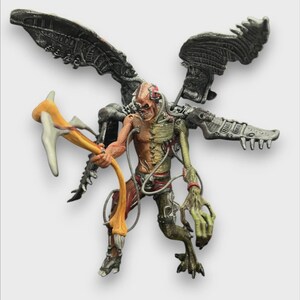 Puede incluir: Figura detallada de una criatura cyborg con alas mecánicas y un arma. La figura tiene una mezcla de rasgos humanos y robóticos, con carne expuesta y componentes metálicos. Sostiene un arma amarilla y blanca.