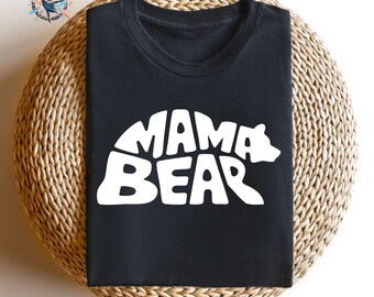 May include: A black t-shirt featuring a white graphic print of the text MAMA BEAR, where the letters are stylized to form the silhouette of a bear. The design is centered on the chest of the shirt, which has a crew neckline and short sleeves.