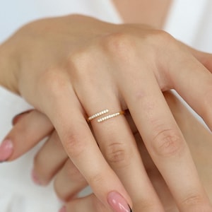 May include: A gold ring with a double row of small, clear stones. The ring is worn on the middle finger of a hand with manicured nails.