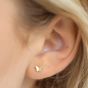 May include: A close-up of a person's ear with a small gold butterfly stud earring.