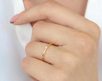 May include: A delicate gold ring with a single small, clear gemstone set in the center.