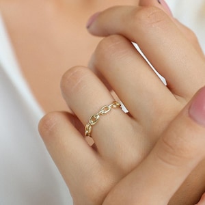 Puede incluir: Un anillo de cadena de oro se usa en un dedo. El anillo está hecho de pequeños eslabones conectados. El anillo es una joya simple y elegante. El anillo se muestra en la mano de una persona.