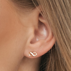 May include: A pair of gold infinity symbol earrings with small clear stones set into the design.