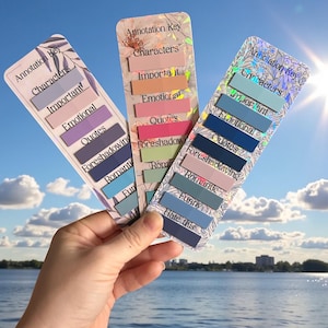 Peut inclure: Trois marque-pages colorés avec des clés d'annotation sont présentés sur fond de ciel bleu. Chaque marque-page a un design différent avec des étiquettes de texte telles que "Characters", "Important" et "Quotes". Les marque-pages sont pour annoter des livres.