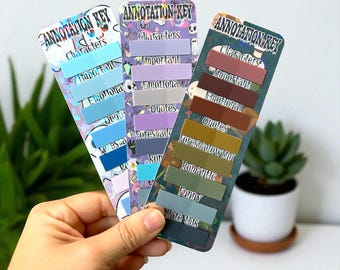 May include: Three colorful annotation key bookmarks with the text "Annotation Key" at the top. Each bookmark has a different color scheme and includes labels like "Characters," "Important," and "Quotes." The bookmarks are held in a hand.