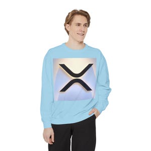 May include: Light blue sweatshirt featuring a black and gold XRP cryptocurrency symbol. The graphic is centered on the chest. The sweatshirt is a solid color and has long sleeves.