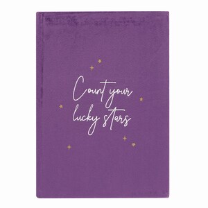 Puede incluir: Diario de terciopelo morado con estrellas doradas y el texto "Count your lucky stars" en cursiva blanca.