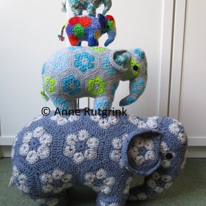 Op de afbeelding: Een stapel van drie gehaakte olifantenbeeldjes. De grootste is blauw met witte bloempatronen. De middelste olifant is veelkleurig en de kleinste is lichtblauw met een bloemmotief. Handgemaakt en decoratief.