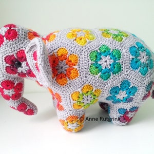 Op de afbeelding: Een handgemaakte gehaakte olifant, versierd met kleurrijke bloempatronen in rood, oranje, geel, groen en blauw. De olifant heeft een grijze basis en een knoop als oog.