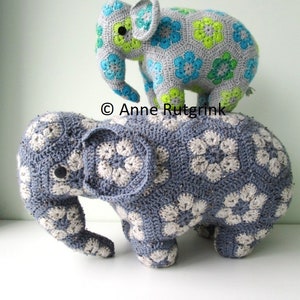 Op de afbeelding: Twee handgemaakte gehaakte olifantenspeeltjes. De grotere olifant is blauw met witte bloempatronen. De kleinere olifant is grijs met blauwe en groene bloempatronen. De speeltjes zijn zacht en knuffelig, perfect voor een kinderkamer.