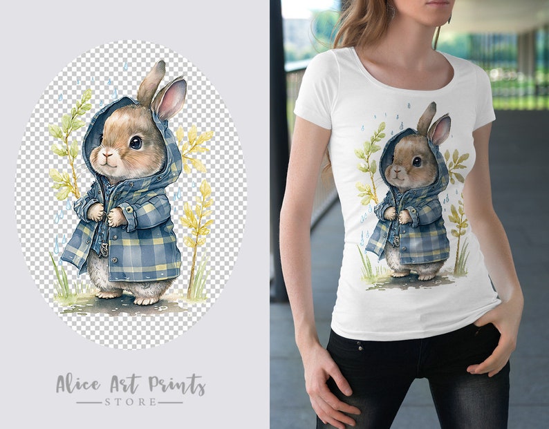 May include: A white t-shirt with a watercolor illustration of a brown rabbit wearing a blue and white plaid raincoat. The rabbit is standing in a field of green grass with yellow flowers. The background is a light blue sky with white raindrops.