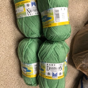 May include: Four skeins of green yarn labeled "Baby Ull Dalegarn" with the text "100% wool, laine, lana, laen, wol, la,  made in Norway by Dale"