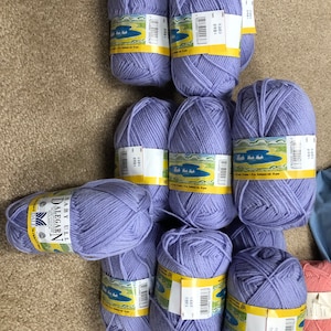 May include: Nine balls of lavender purple yarn with yellow labels. The labels have the text "Baby Ull Dalegarn" and a picture of a lake with swans.