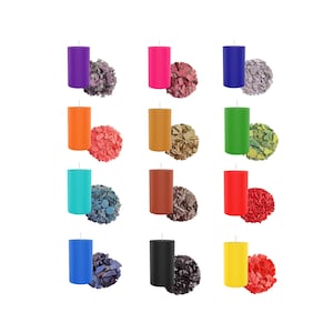 Könnte beinhalten: Zwölf Säulenkerzen in verschiedenen Farben, darunter Lila, Pink, Orange, Braun, Grün, Türkis, Rot, Blau, Schwarz und Gelb. Jede Kerze ist mit einem kleinen Haufen Wachsflocken in der entsprechenden Farbe gepaart.