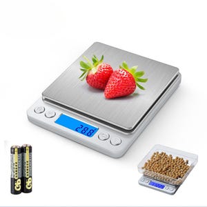 May include: A silver digital kitchen scale with a blue LCD display showing "2.88". The scale has a stainless steel platform and is sitting on a white surface. Two AA batteries are shown next to the scale. The scale is also shown weighing a small bowl of brown beans.