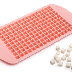 Op de afbeelding: Een roze siliconen ijsblokjesbak met 100 individuele vierkante vormen. De bak is gevuld met kleine witte ijsblokjes.