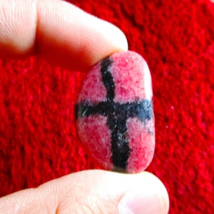 Puede incluir: Una piedra preciosa rosa y negra con un patr&oacute;n de cruz. La piedra es lisa y pulida.