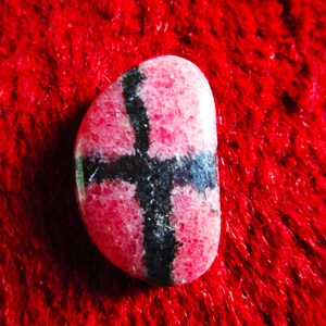 Puede incluir: Una piedra preciosa rosa y negra con un patr&oacute;n de cruz. La piedra preciosa es lisa y pulida.