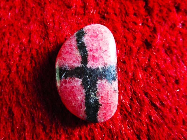 Puede incluir: Una piedra preciosa rosa y negra con un patr&oacute;n de cruz. La piedra preciosa es lisa y pulida.