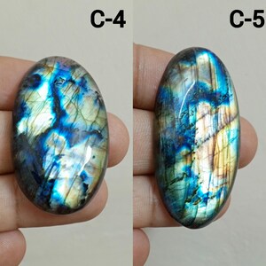 Peut inclure: Deux pierres de labradorite polies, &eacute;tiquet&eacute;es C-4 et C-5. Les pierres pr&eacute;sentent des reflets iris&eacute;s de bleu, de vert et d'or dans une matrice sombre. Les formes ovales et allong&eacute;es mettent en valeur les motifs naturels.