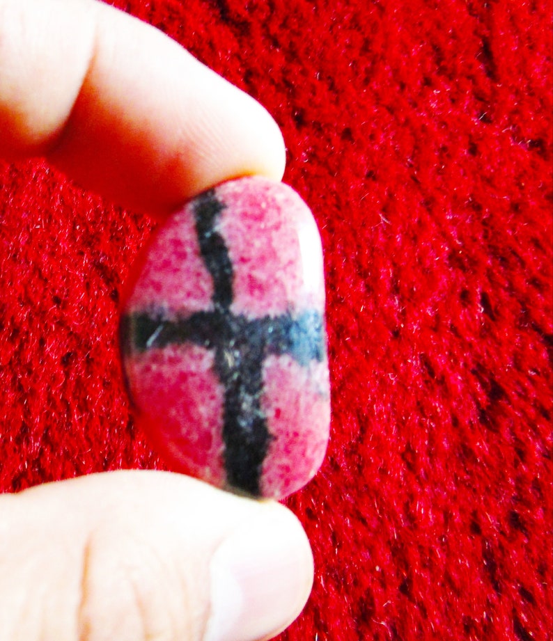 Puede incluir: Una piedra preciosa rosa y negra con un patr&oacute;n de cruz. La piedra es lisa y pulida.