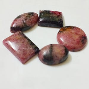 Puede incluir: Cinco piedras preciosas cabujón de color rosa y negro en una variedad de formas, incluyendo ovalada, rectangular y redonda.
