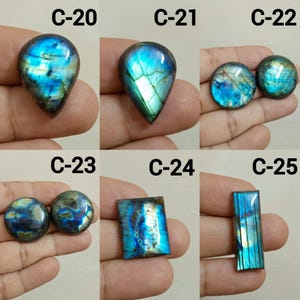 Peut inclure: Collection de pierres pr&eacute;cieuses de labradorite polies de diff&eacute;rentes formes, dont des gouttes, des ronds et des rectangles. Les pierres pr&eacute;sentent des reflets iris&eacute;s bleus, verts et dor&eacute;s. Chaque pierre est &eacute;tiquet&eacute;e avec un "C" suivi d'un num&eacute;ro.
