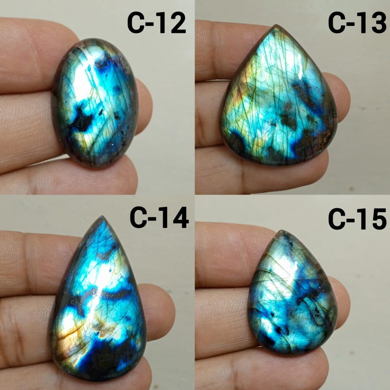 Peut inclure: Quatre pierres pr&eacute;cieuses de labradorite polies, de formes ovales et en goutte. Les pierres pr&eacute;sentent des reflets iris&eacute;s bleus, verts et dor&eacute;s. Chaque pierre est &eacute;tiquet&eacute;e avec un "C" suivi d'un num&eacute;ro : C-12, C-13, C-14 et C-15. Les pierres sont tenues dans une main.