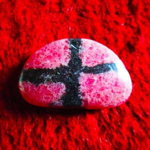 Puede incluir: Una piedra rosa y negra con un patr&oacute;n de cruz. La piedra es lisa y tiene una superficie texturizada.