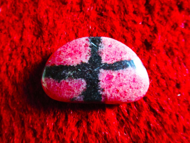 Puede incluir: Una piedra rosa y negra con un patr&oacute;n de cruz. La piedra es lisa y tiene una superficie texturizada.