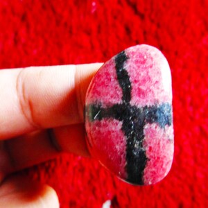 Puede incluir: Una piedra preciosa rosa y negra con un patr&oacute;n de cruz. La piedra preciosa es lisa y pulida.