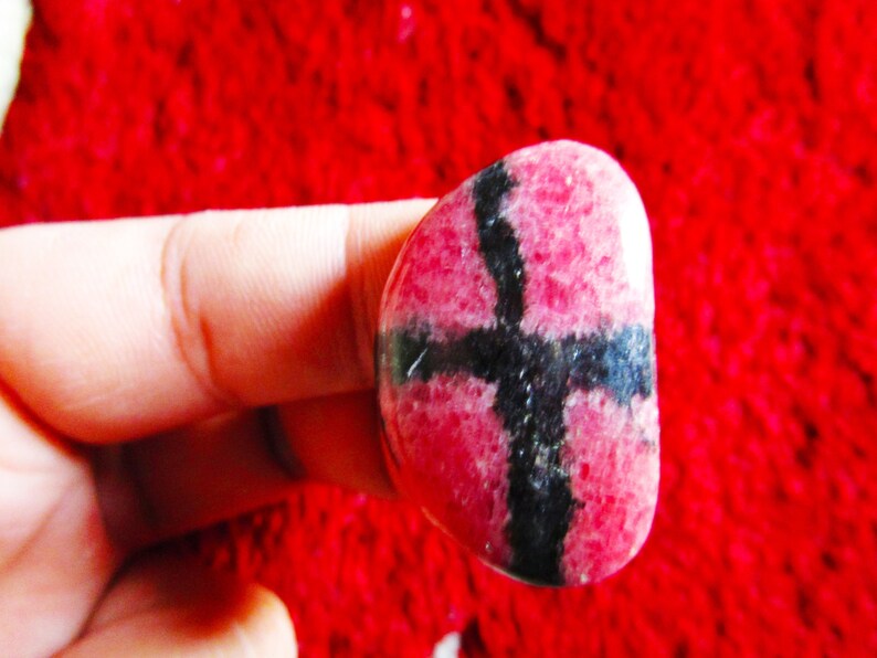 Puede incluir: Una piedra preciosa rosa y negra con un patr&oacute;n de cruz. La piedra preciosa es lisa y pulida.