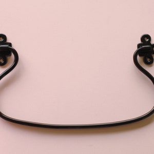 May include: Black metal hook with a decorative design on each end. The hook is curved and has a smooth finish.