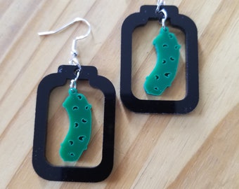 May include: A pair of black and green pickle earrings. Each earring features a green pickle charm hanging inside a black rectangle.