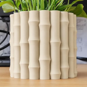 May include: A cylindrical plant pot with a matte beige finish, featuring a textured exterior surface composed of vertical, segmented bamboo-like stalks arranged in a repeating pattern around the entire circumference of the container.