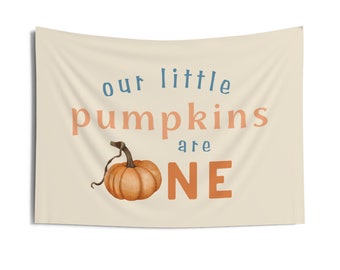 May include: A beige banner with the text "our little pumpkins are one" in blue and orange. A small orange pumpkin is illustrated next to the text.