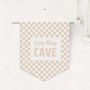 Può includere: Uno stendardo bianco con un motivo a scacchi marroni e il testo "Tiny Man CAVE" in un riquadro bianco.