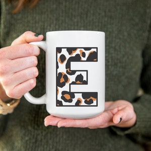 May include: White ceramic mug with a large letter "E" printed on the front. The letter is filled with a leopard print pattern in brown, black, and white.