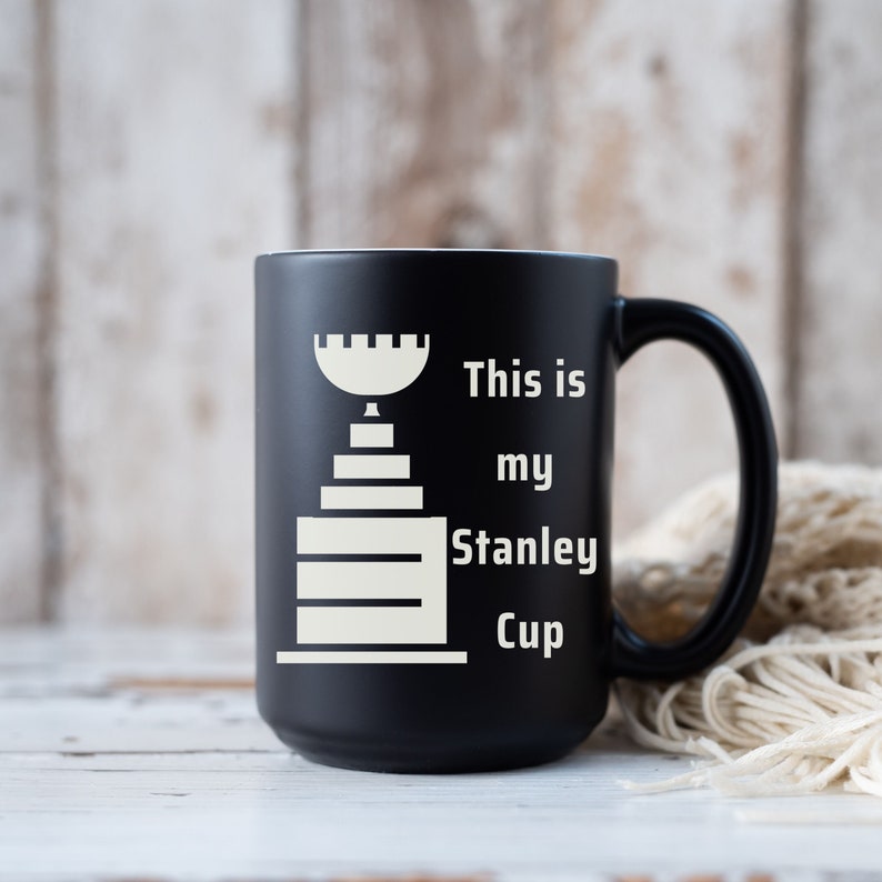 Pu&ograve; includere: Tazza in ceramica nera con una grafica bianca del trofeo della Stanley Cup e il testo "This is my Stanley Cup".