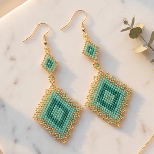 Peut inclure: Une paire de boucles d'oreilles pendantes composées d'un petit élément en perles en forme de losange relié à une pièce plus grande en forme de losange. Les perles sont dans des tons bleu sarcelle et vert, avec des perles dorées et des crochets dorés.