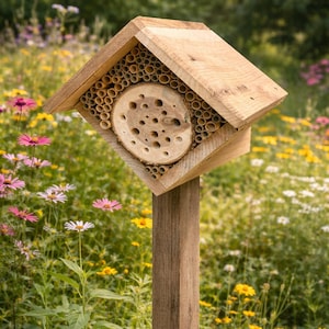 May include: A wooden bee house featuring a peaked roof, a central circular log section with drilled holes, and surrounding bamboo tubes. The structure is mounted on a vertical wooden post, providing a habitat for solitary bees and pollinators.
