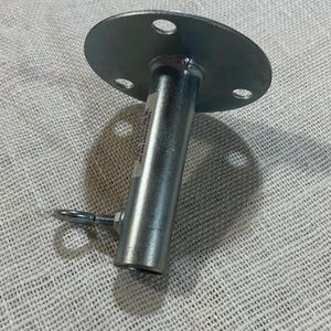 Könnte beinhalten: Eine silberfarbene Metallstange mit einer kreisförmigen Oberseite mit vier gleichmäßig verteilten Löchern. Die Stange hat einen zylindrischen Körper und ein kleineres, mit Gewinde versehenes Ende mit einem angebrachten Ring. Ein Etikett ist an der Stange angebracht.