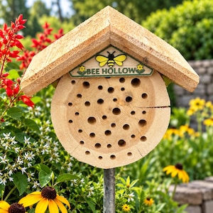 May include: A circular wooden bee house with a peaked roof, featuring numerous drilled holes of varying sizes. A triangular sign attached to the front displays a yellow and black bee graphic, the text BEE HOLLOW, and small yellow flowers.