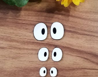 May include: A set of six white googly eyes with black pupils, in three different sizes. The eyes are arranged in three rows of two, with the largest eyes at the top and the smallest eyes at the bottom.