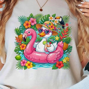 May include: A light-colored t-shirt featuring a cartoon duck wearing heart-shaped sunglasses and a straw hat, floating on a pink flamingo floatie. The duck is holding a cocktail. Tropical flowers, leaves, and a toucan surround the duck.