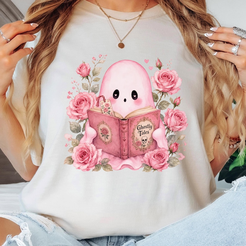 Woman wearing pink ghost reading book t-shirt. Coquette Halloween floral ghost design, spooky season sublimation shirt graphic.