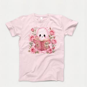 Pink ghost reading book sublimation design on t-shirt. Cute coquette Halloween ghost with flowers, bookish spooky season graphic.