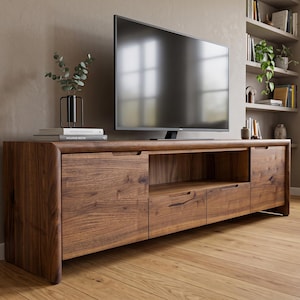 Op de afbeelding: Een lang, laag mediameubel gemaakt van donker walnoothout met afgeronde hoeken. De unit is voorzien van twee zijkasten met dichte deuren, twee centrale lades en een open schapruimte. Een flatscreen-televisie staat bovenop het meubel.